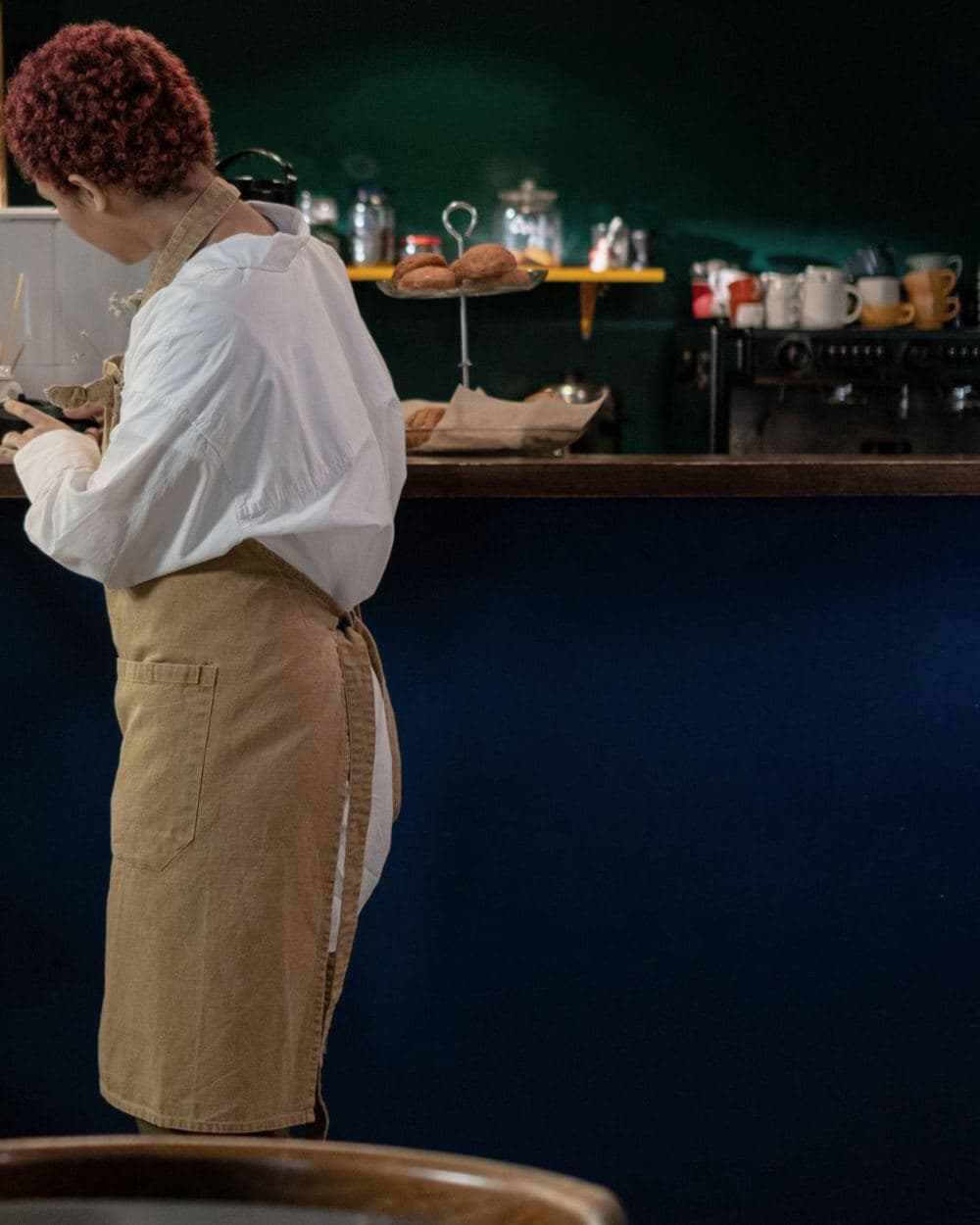 Atendente de avental preparando um pedido no balcão de uma cafeteria.